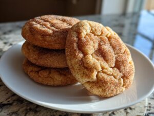 A stack of four soft, crinkled cinnamon cookies coated in sugar and spice, resting on a white plate.