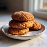 A stack of three golden brown cinnamon cookies generously coated in cinnamon sugar, resting on a small plate.