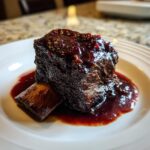 A single, perfectly cooked braised short ribs piece covered in a dark, glossy sauce on a white plate.