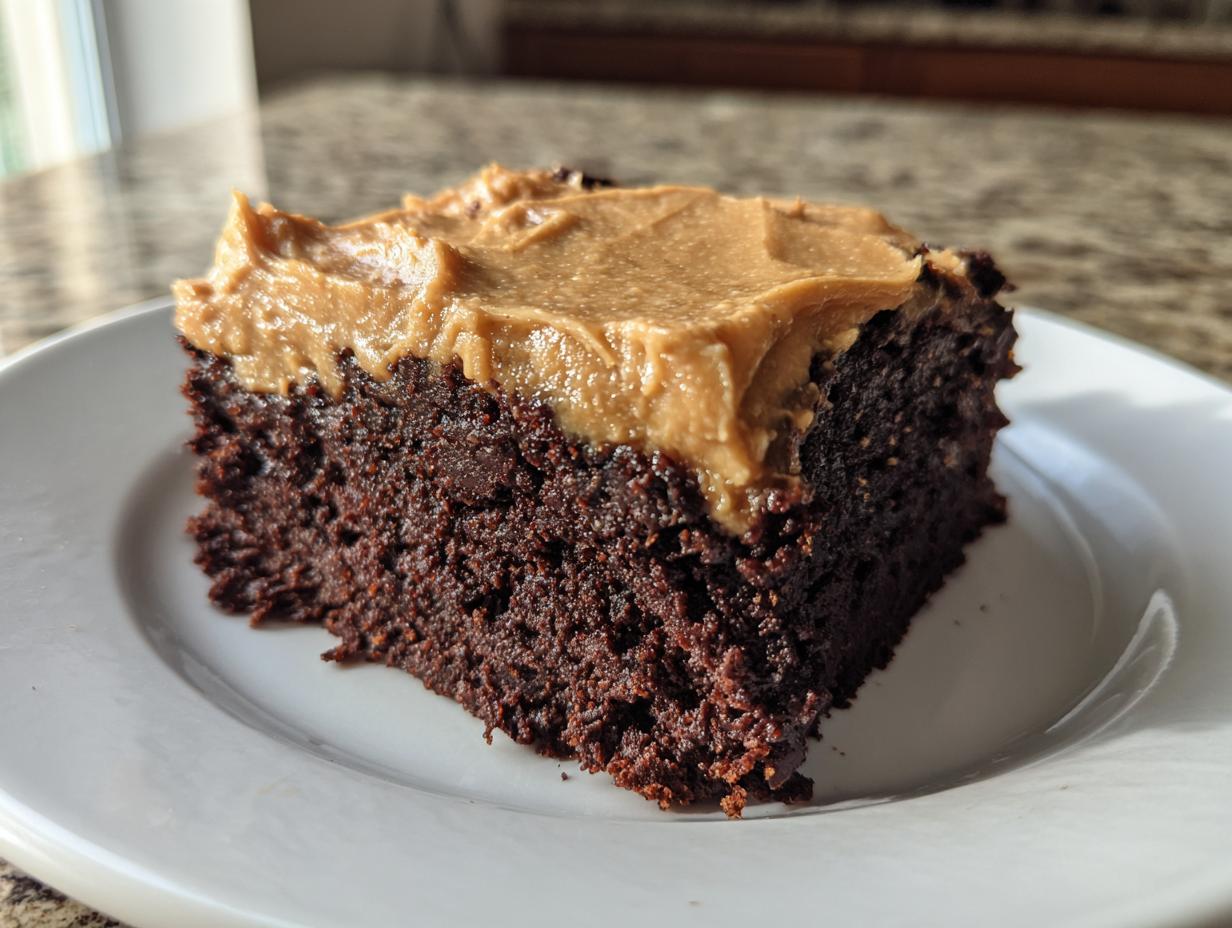 A close-up of a rich, dark chocolate slice of banana bread brownies topped with creamy peanut butter frosting.