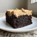 A close-up of a rich, dark chocolate banana bread brownies square topped with thick peanut butter frosting.