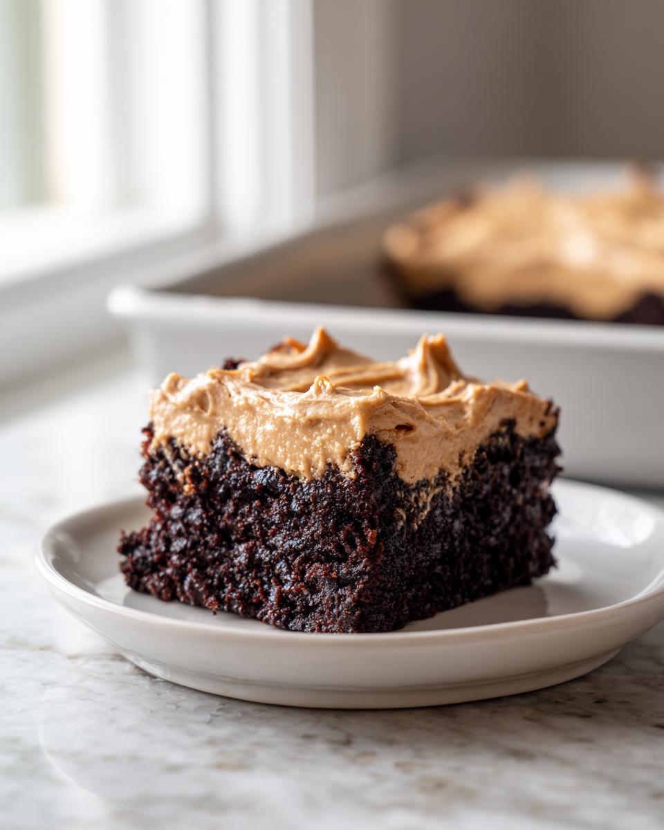 A square slice of rich, dark banana bread brownies topped with thick peanut butter frosting on a white plate.