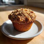 A close-up of a single, golden brown banana nut muffins topped with a generous, crunchy streusel topping.