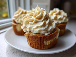 A close-up of one amazing banana pudding cupcake topped with a generous swirl of creamy frosting on a white plate.