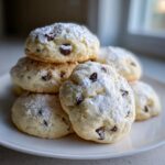 A delicious stack of soft cannoli cookies dusted heavily with powdered sugar and studded with mini chocolate chips.