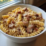 Close-up of creamy kielbasa pasta made with fusilli noodles and chunks of browned sausage in a white bowl.